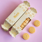 Two decorated Bluebells Bakery biscuit boxes on a pastel pink background, with several round golden biscuits placed beside them.