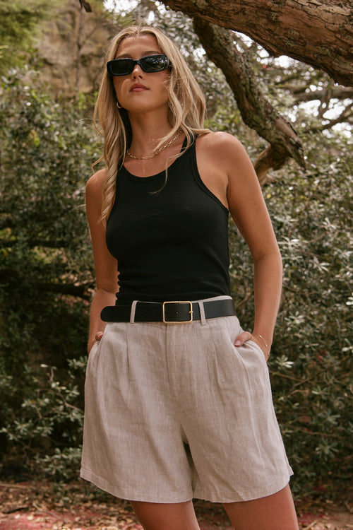 model wearing beige linen shorts and a black cotton singlet