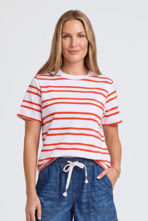 A woman modeling a white short-sleeve crewneck t-shirt with thin orange horizontal stripes, paired with blue denim drawstring shorts, against a light gray studio background.