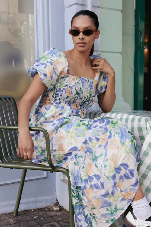 model is outside and wears and blue and orange floral maxi dress with sneakers