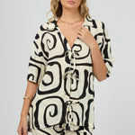 cream buttonless shirt with bold black swirl print and multiple front tie fastenings, worn with gold jewellery