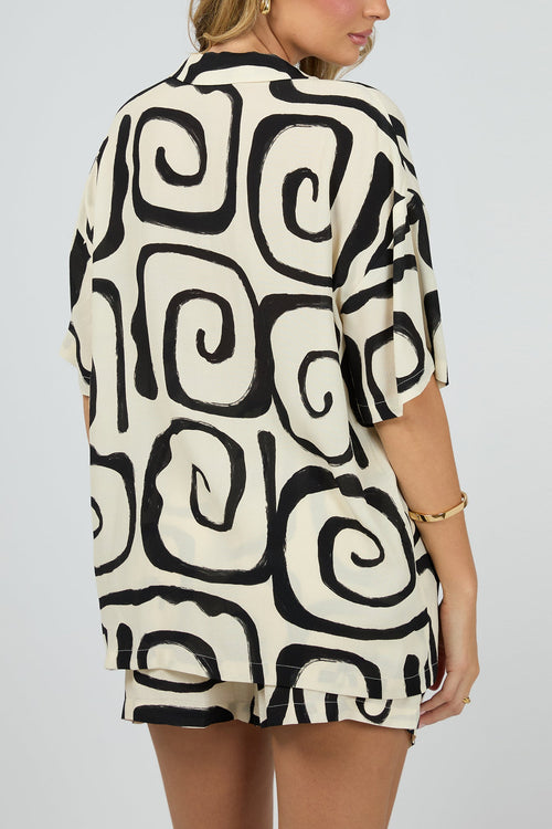 cream buttonless shirt with bold black swirl print and multiple front tie fastenings, worn with gold jewellery