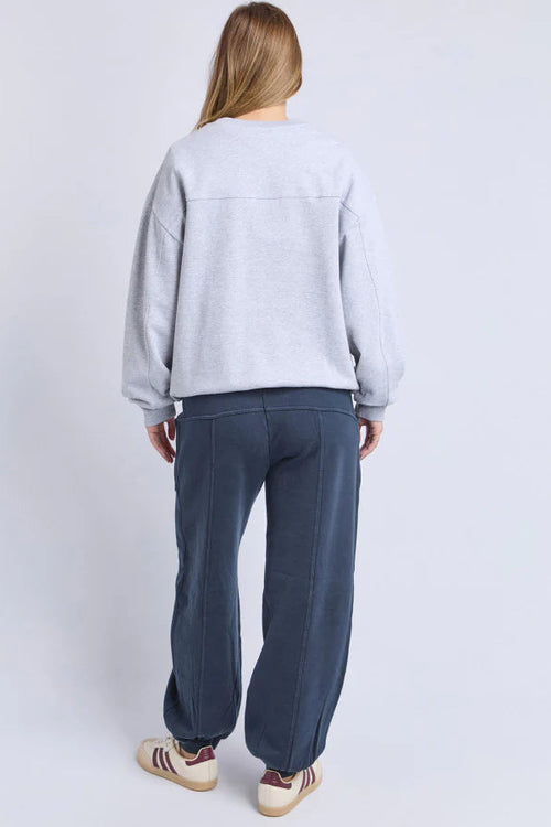 Person wearing a light gray sweatshirt and dark blue pants on a white background