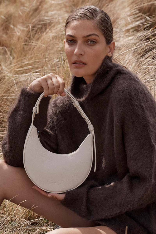 Woman holding a white handbag in a field of tall grass