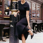 model poses on the sidewalk in a long black rib kit dress with short sleeves and black heels