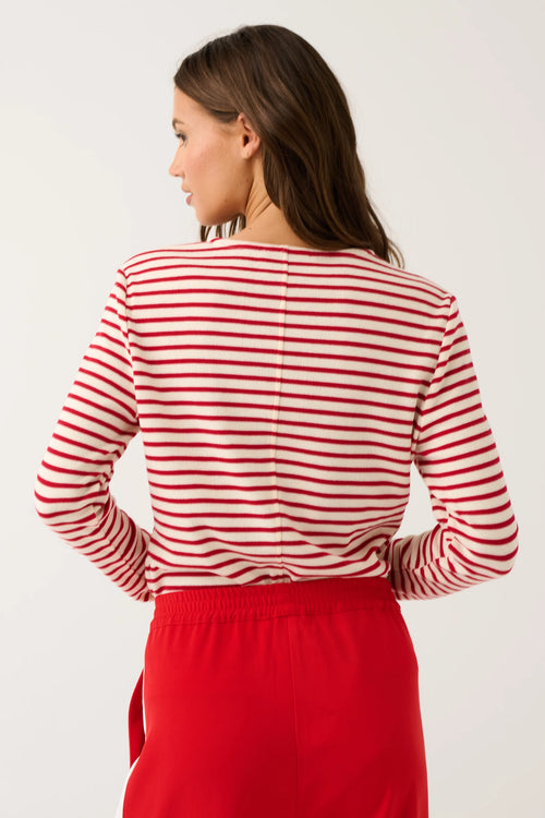 A woman shown from the back wearing a red and white horizontally striped long-sleeve top and a solid red skirt, against a plain light gray studio background.